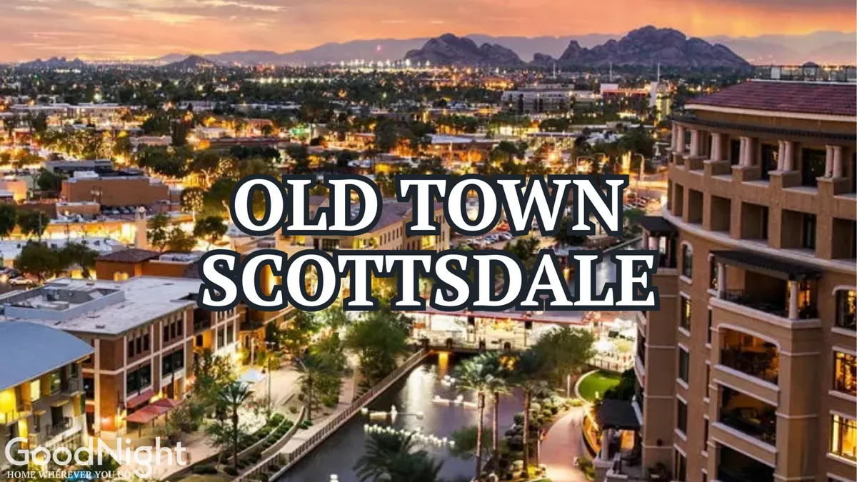 A sweeping view of Old Town Scottsdale as dusk falls, with city lights twinkling, mountains silhouetted in the background, and water features reflecting the vibrant energy of the area. People can be seen strolling, dining, and enjoying the nightlife.