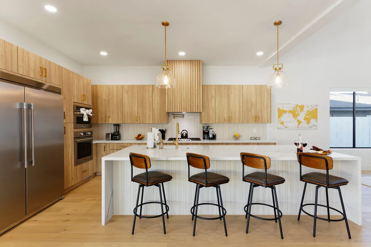 A contemporary kitchen with a spacious island, sleek appliances, pendant lighting, and bar stools, designed for both preparing meals and socializing. The space looks meticulously organized and inviting.
