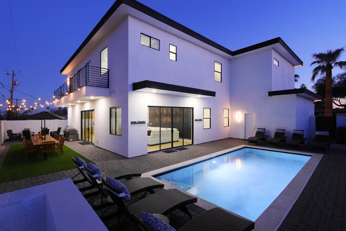 This image captures a sparkling swimming pool surrounded by an outdoor seating area and a dining table, all set against a backdrop of modern architecture. String lights create a festive and inviting atmosphere, perfect for social gatherings and poolside relaxation.