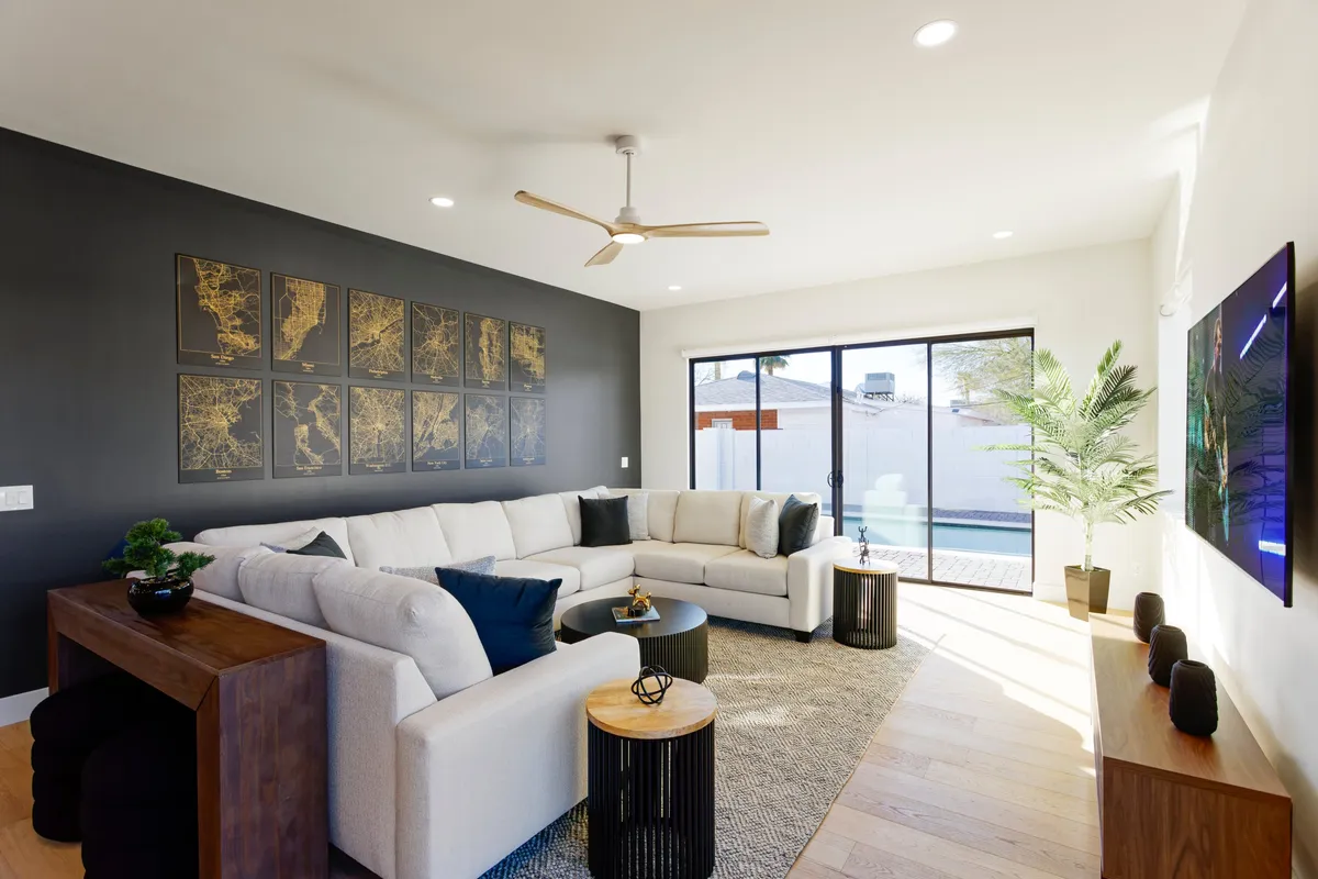 A spacious main living area featuring a large plush sectional sofa, contemporary artwork on the wall, a tall potted plant, and sliding glass doors that offer abundant natural light. The layout is ideal for group relaxation, movie nights, and lively socializing.