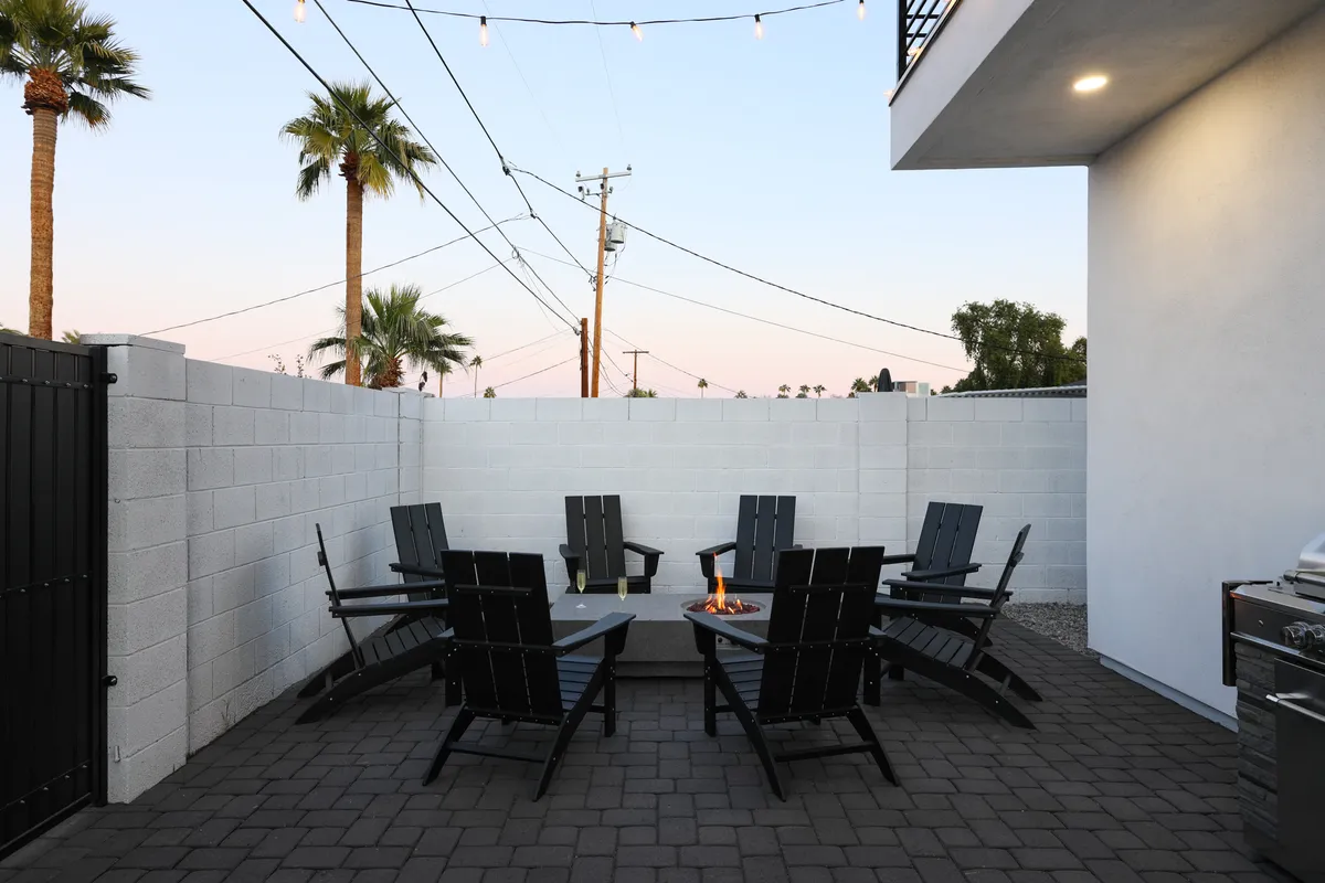 An inviting outdoor fire pit area with Adirondack chairs, palm trees, and string lights, creating a cozy communal space for evening gatherings and safe, memorable family experiences under the stars.