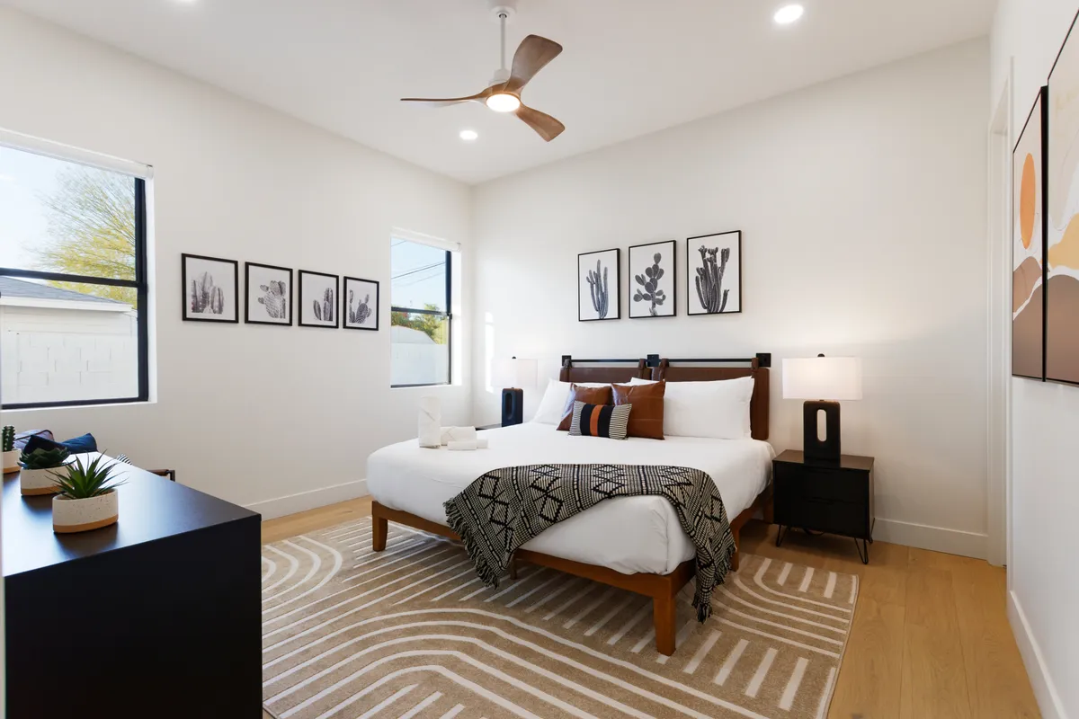 A cozy king bedroom with decorative pillows, modern artwork, nightstands topped with lamps, and large windows streaming in natural light. The arrangement is inviting and plush, suggesting a private, restful atmosphere for guests.