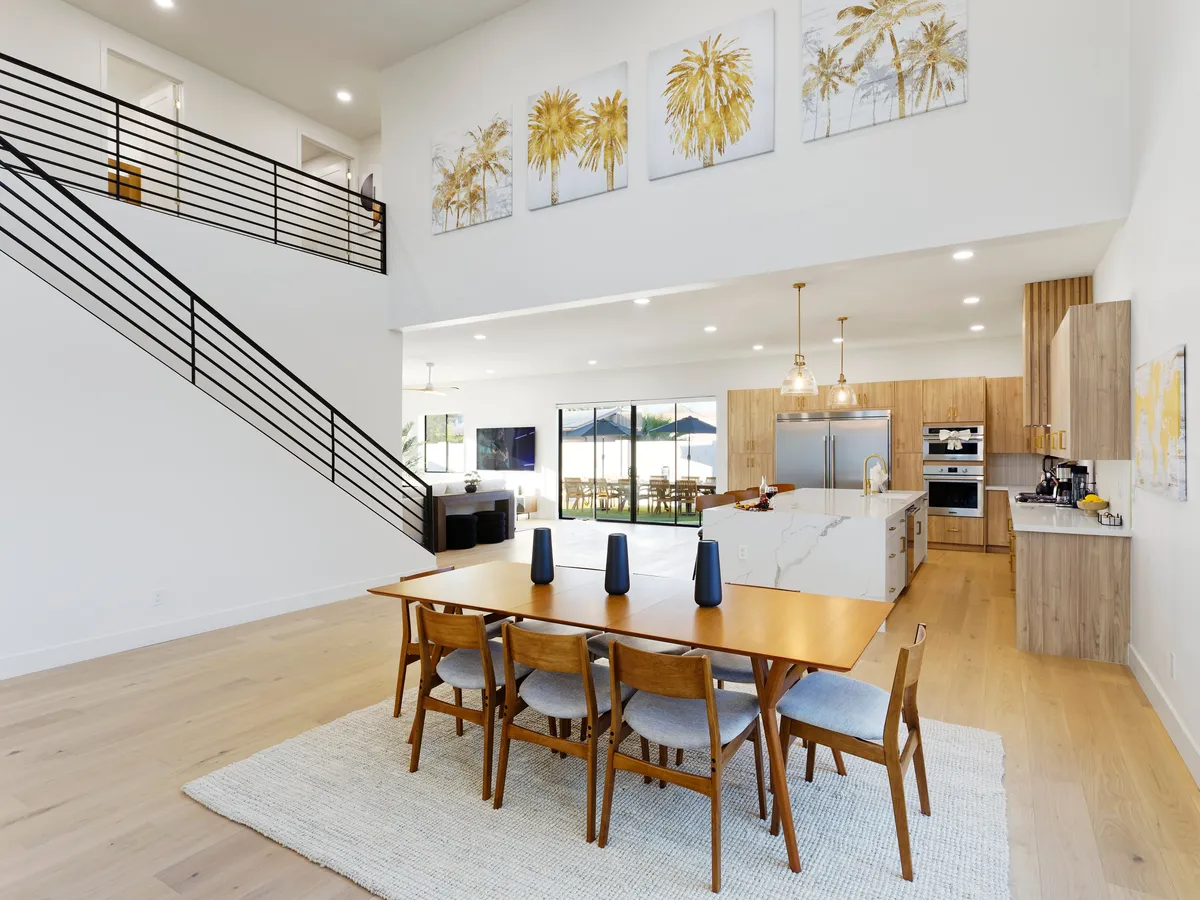 A welcoming dining area seamlessly connected to a modern kitchen, with a large dining table set for eight, contemporary artwork adorning the wall, and stairs leading to the upper floor. The open layout fosters an inviting environment for family dinners and festive occasions.