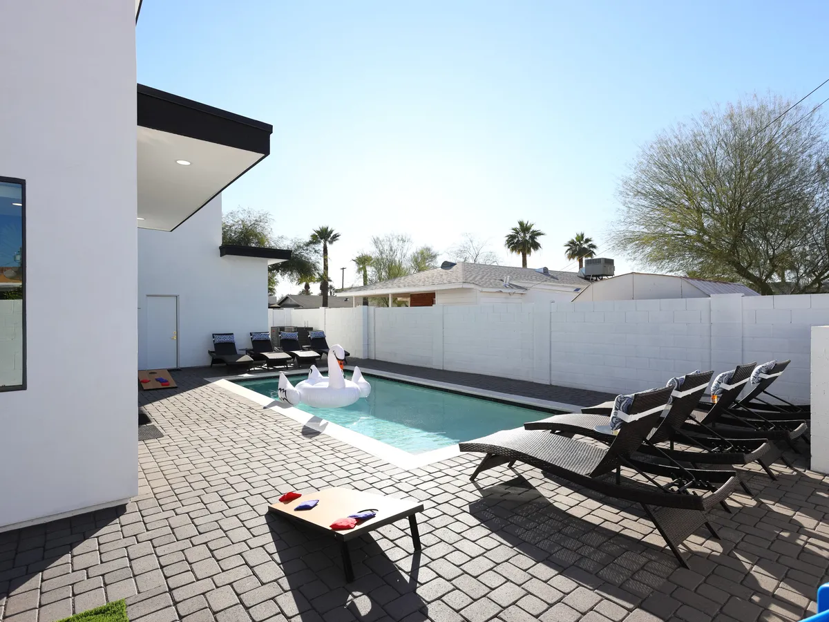 A vibrant exterior shot of a swimming pool with lounge chairs, an inflatable swan, and a paved patio. The area is bathed in cheerful sunlight, promising fun, relaxation, and opportunities for families to socialize or unwind together.