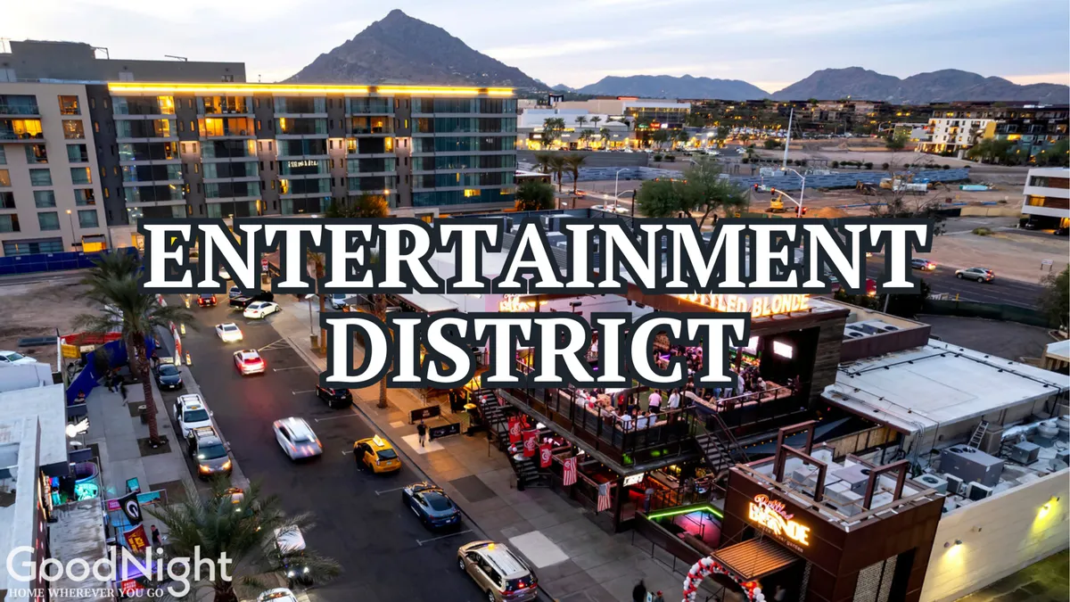 A dynamic street scene in the Entertainment District featuring bold signage, bustling traffic, outdoor seating, and a scenic mountain backdrop. The street is filled with people enjoying dining and live entertainment.